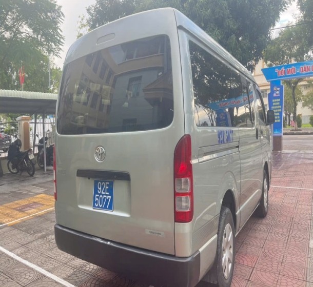 Hình ảnh mặt bên của một xe ô tô cũ 16 chỗ Toyota Hiace màu trắng, cho thấy toàn bộ chiều dài xe và các cửa sổ.