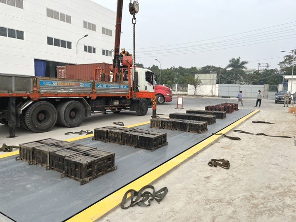 Một kỹ thuật viên đang hiệu chuẩn trạm cân điện tử bằng cách đặt các quả cân chuẩn, công việc quan trọng để tránh những lỗi của xe ô tô khi cân tải trọng