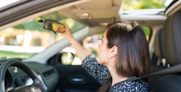 Người lái đang ngồi vào ghế xe ô tô, điều chỉnh gương chiếu hậu bên trong xe và thắt dây an toàn để chuẩn bị khởi động xe ô tô.