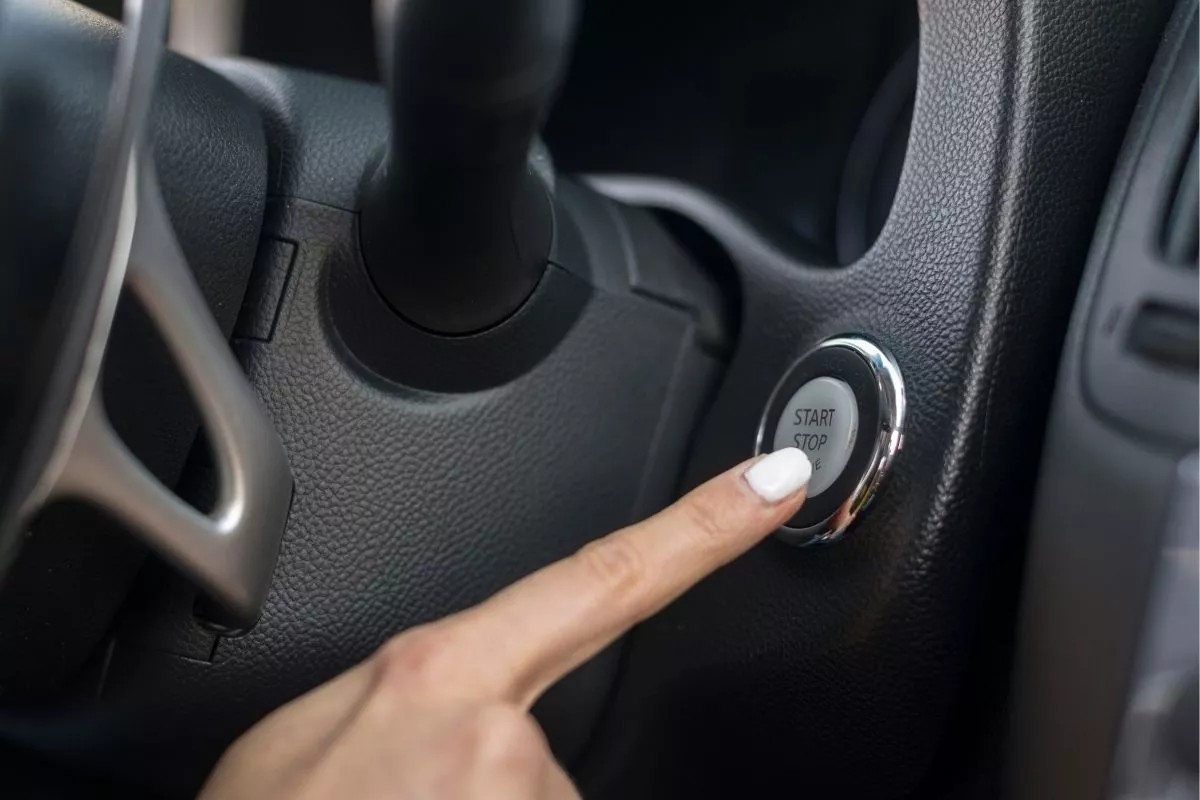 Bàn tay đang nhấn vào nút Engine Start Stop trên bảng điều khiển xe ô tô để khởi động động cơ.