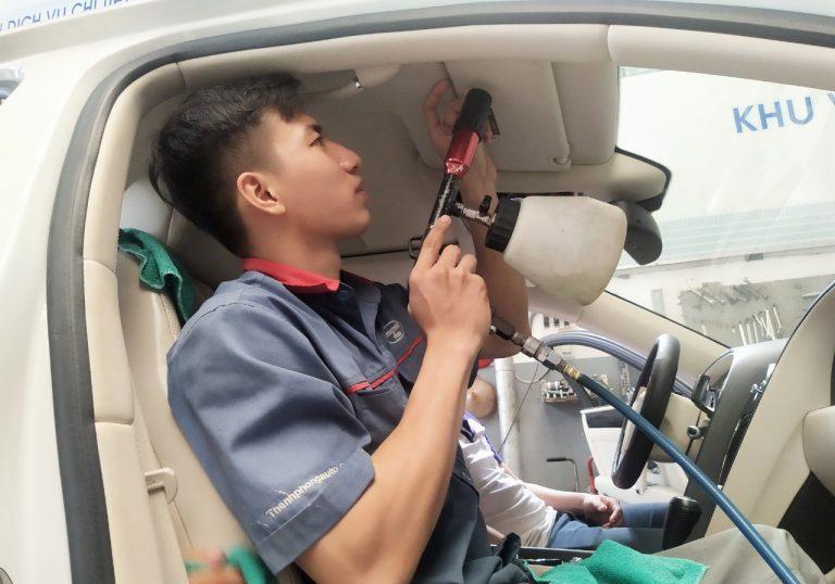 Thợ chuyên nghiệp đang vệ sinh trần xe ô tô bằng dung dịch và khăn mềm