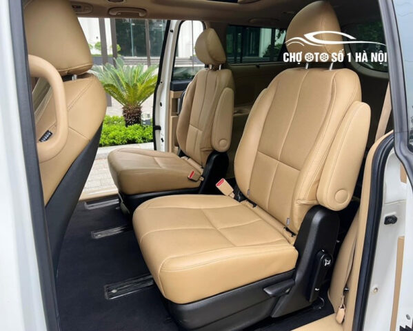 Chiếc xe Kia Sedona 7 chỗ cũ màu đen được đậu trong một bãi đậu xe, với ánh nắng mặt trời phản chiếu trên bề mặt bóng loáng