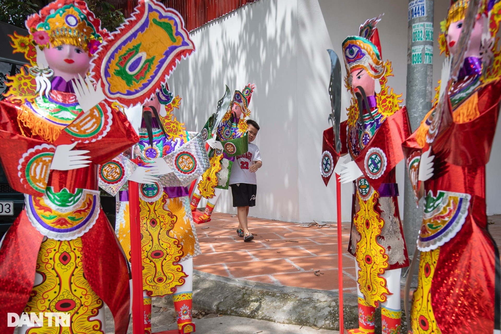 Một người phụ nữ ngồi giữa không gian làm việc truyền thống, bao quanh bởi các sản phẩm vàng mã, cho thấy hoạt động sản xuất tại thủ phủ xe ô tô giấy