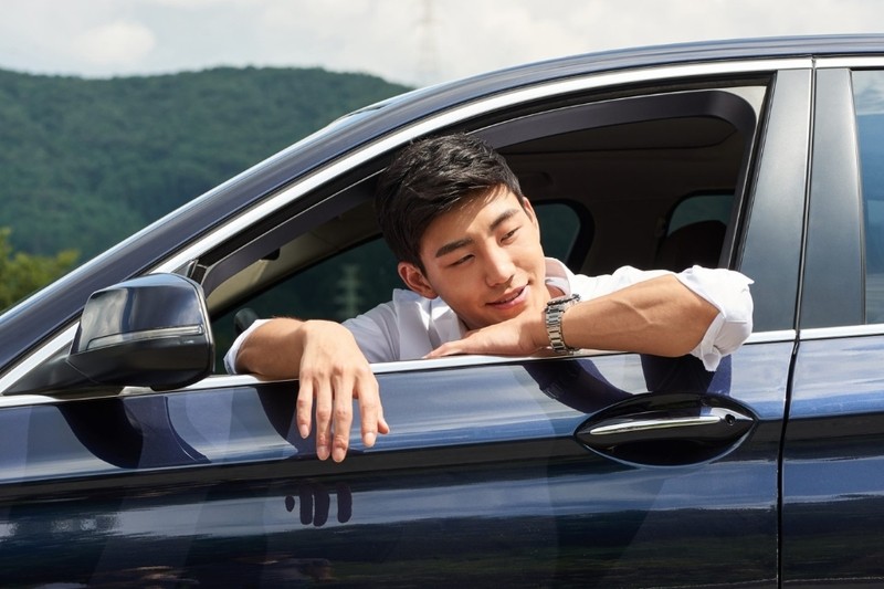 Một người đàn ông đang ngồi trong chiếc xe sang trọng, tay đặt trên vô lăng và nhìn thẳng vào ống kính, thể hiện sự tập trung và đẳng cấp khi chụp ảnh với xe ô tô
