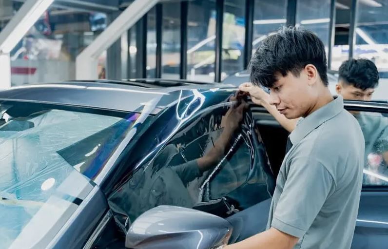 Kỹ thuật viên đang dán phim cách nhiệt cho cửa kính xe ô tô, giải pháp chống nóng trần xe ô tô và bảo vệ nội thất hiệu quả