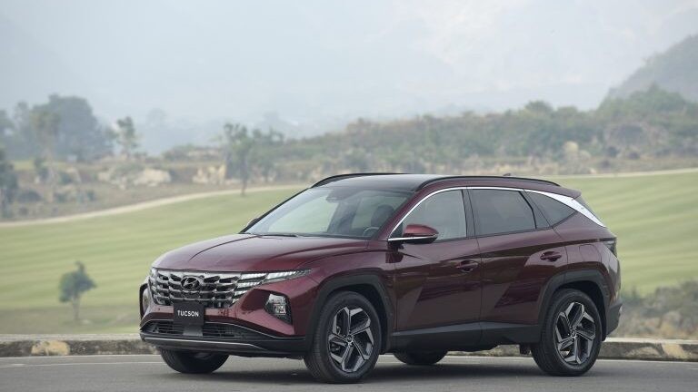 Một chiếc Hyundai Tucson màu xám bạc đang di chuyển trên đường, thể hiện sự năng động và hiện đại của một mẫu SUV tầm trung được ưa chuộng.