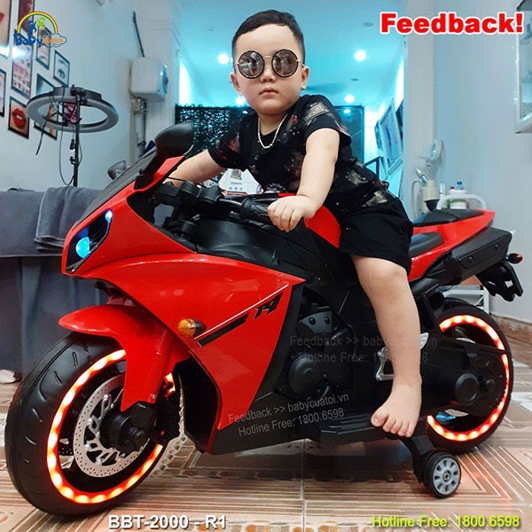 Bé trai đang chơi xe máy điện màu xanh trên sân, rèn luyện kỹ năng lái xe máy ô tô cơ bản