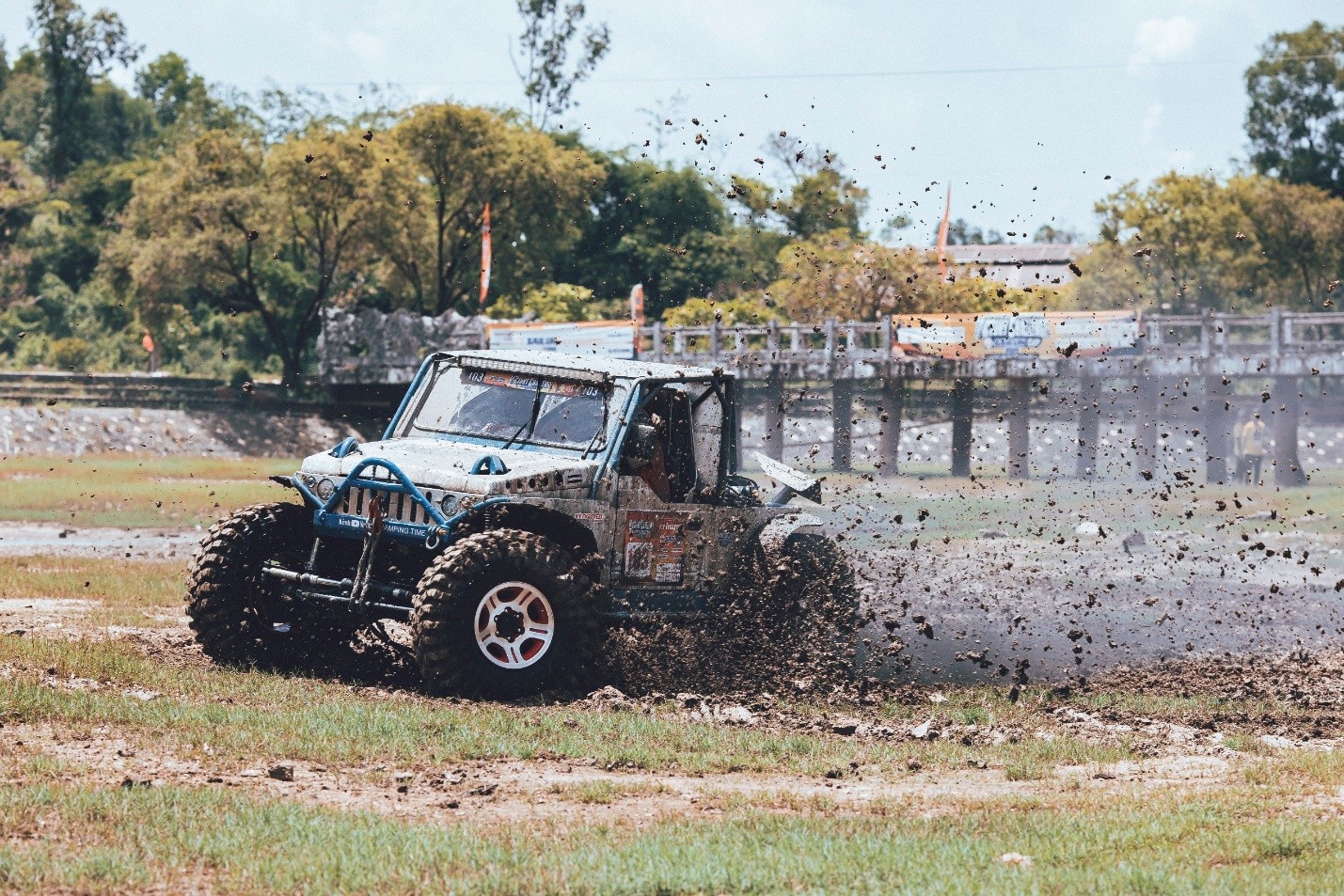 Chiếc xe off-road màu xanh mạnh mẽ vượt qua chướng ngại vật trên đường đua bùn lầy