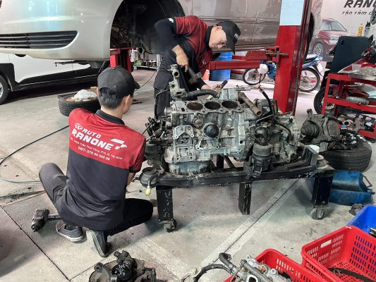 Kỹ thuật viên đang kiểm tra động cơ tại một garage ô tô, minh họa dịch vụ sửa xe ô tô bên ngoài hãng.