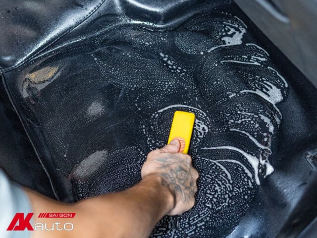 Người dùng đang vệ sinh sàn xe ô tô bằng bàn chải để loại bỏ bụi bẩn